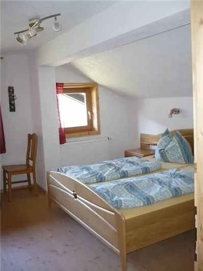 Ein gemütliches Schlafzimmer mit einem Doppelbett und blauem Bettzeug. Es gibt ein Fenster und einen Stuhl in der Ecke.