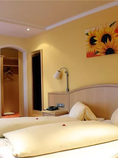 Een heldere hotelkamer met een tweepersoonsbed en gele muren. Een gezellige zithoek en een schilderij van zonnebloemen sieren de kamer.