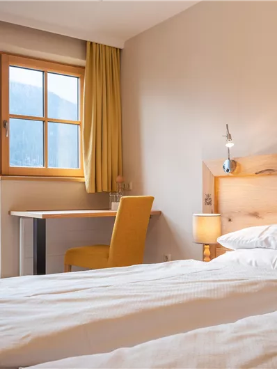 Ein gemütliches Schlafzimmer mit zwei Betten und Holzmöbeln. Der Raum hat ein Fenster mit einem schönen Blick nach draußen und ist hell erleuchtet.