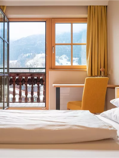 Ein gemütliches Zimmer mit einem großen Fenster und einem Balkon, der einen Blick auf die Berge bietet. Die Einrichtung ist modern und freundlich, ideal für einen entspannten Aufenthalt.