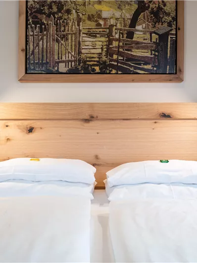 Ein gemütliches Schlafzimmer mit zwei Einzelbetten und einer Holz Kopf-teil. An den Wänden hängen Lampen und ein Kunstwerk.