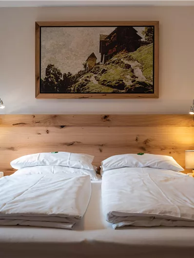 Ein gemütliches Schlafzimmer mit zwei Betten und einer Holzverkleidung. An der Wand hängt ein Gemälde, das eine ruhige Landschaft zeigt.