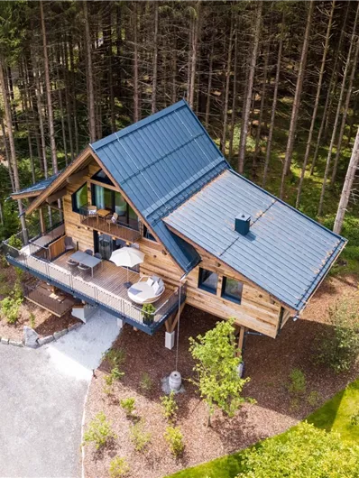 Ein modernes Holzhaus umgeben von Bäumen in einer ruhigen Naturumgebung. Die Veranda lädt zum Entspannen ein.