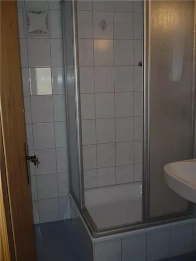 Ein Badezimmer mit einer Duschkabine und einem Waschbecken. Die Wände sind gefliest und die Tür aus Holz.