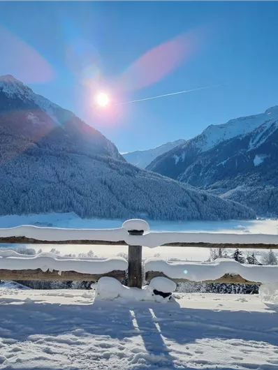 A snowy mountain landscape under a clear blue sky. The sun shines brightly and casts shadows on the snow.