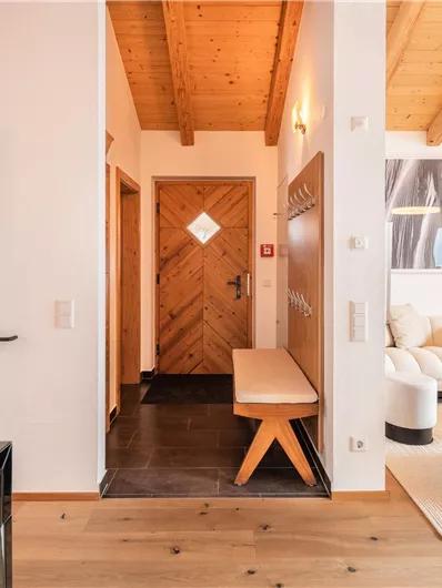 Ein einladender Flur mit Holzbalkendecke und modernem Design. Rechts befindet sich ein gemütlicher Wohnbereich mit hellen Möbeln.