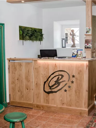 Ein einladender Empfangsbereich mit Holztheke und grünen Akzenten. Gemütliche Sitzgelegenheiten und eine künstlerische Dekoration schaffen eine freundliche Atmosphäre.