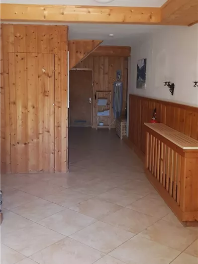 Ein heller Flur mit Holzwänden und einem fliesenbedeckten Boden. Auf der rechten Seite befindet sich eine Holzablage.