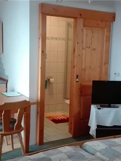 Een eenvoudige kamer met een tafel, stoel en een televisie. De kleine keuken is goed uitgerust, en de badkamer is achter een deur zichtbaar.