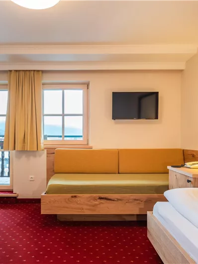 Ein gemütliches Hotelzimmer mit einem Doppelbett und einem Sitzbereich. Das Zimmer hat einen Fernseher und große Fenster mit Blick nach draußen.