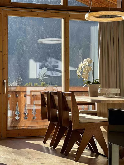 Ein helles Esszimmer mit einem Holztisch und modernen Stühlen. Große Fenster bieten einen Blick nach draußen und lassen viel Licht herein.