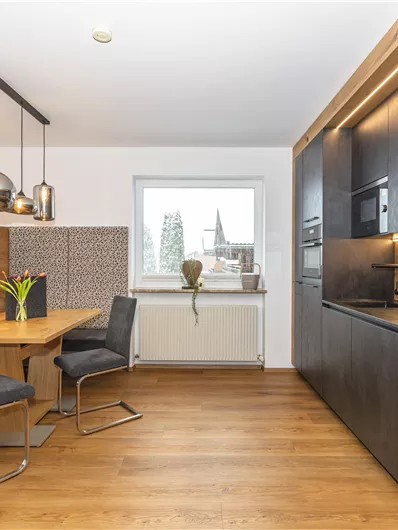 Een moderne keuken met houten vloer en elegante meubels. Een eetgedeelte met een ronde tafel en stoelen is goed verlicht.