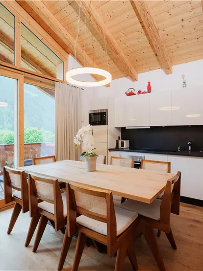 Eine moderne Küche mit Holzdecke und großen Fenstern. Der Essbereich ist hell und einladend, mit einem Tisch und Stühlen.