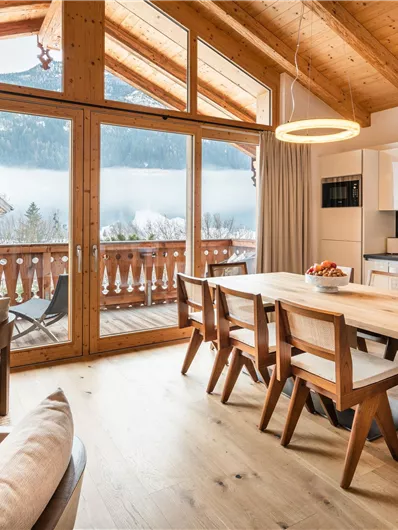 Ein modernes, helles Wohnzimmer mit Holzveranda und großen Fenstern. Der Raum ist mit einem Esstisch und stilvollen Möbeln ausgestattet.