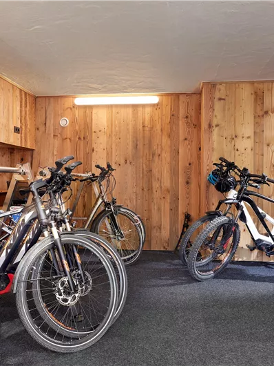 Een fietsenruimte met meerdere fietsen en een houten wand. De ruimte heeft een gestructureerde muur en voldoende licht.
