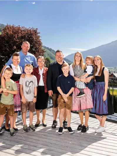 Eine Gruppe von zehn Personen steht auf einer Terrasse mit Blick auf die Berge. Sie tragen traditionelle Trachten und lächeln in die Kamera.