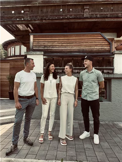 Four people are smiling in front of a building. They are wearing fashionable summer clothes and seem to be enjoying a relaxed atmosphere.