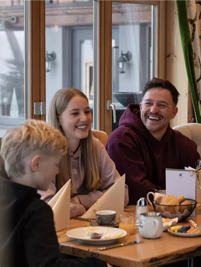 Eine Gruppe von vier Personen sitzt an einem Tisch in einem gemütlichen Restaurant. Sie lachen und genießen ihr Essen in einer warmen Atmosphäre.