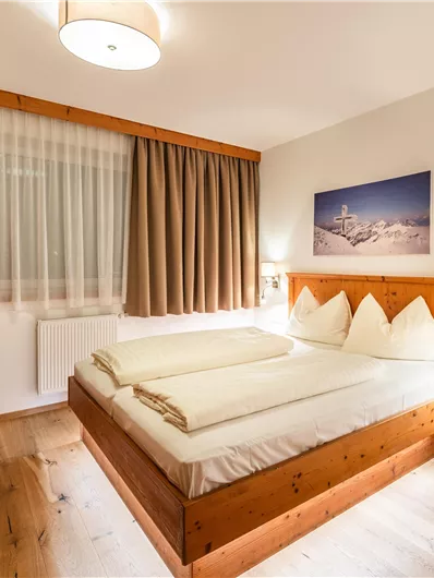 Ein gemütliches Schlafzimmer mit zwei Betten und einem Etagenbett. Es hat warme Holzverkleidungen und ein großes Fenster mit Vorhängen.
