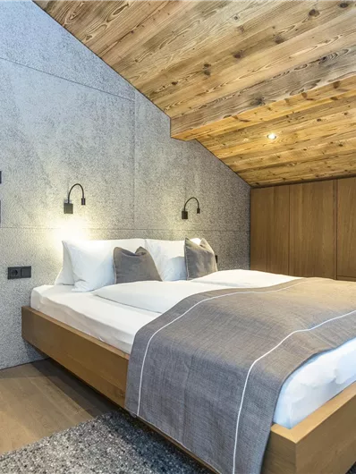 Een moderne slaapkamer met houten plafonds en zachte verlichting. De inrichting is eenvoudig en elegant, met een groot bed en een kast van hout.