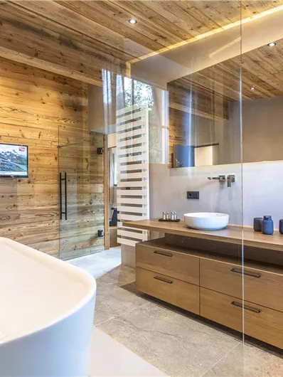 Een moderne badkamer met houten wanden en een grote raampartij. Er is een vrijstaand bad, twee wastafels en een elegante douche.