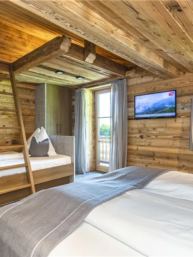 Een gezellige kamer met houten bekleding en twee bedden. Aan de muur hangt een televisie en grote ramen laten veel licht binnen.