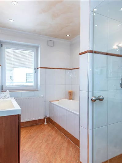 Een moderne badkamer met een douche en een bad. Helle tegels en houten details zorgen voor een uitnodigende sfeer.