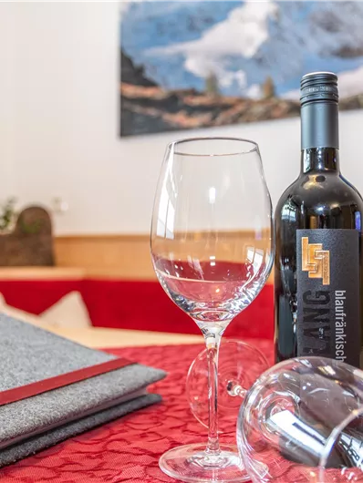 Een elegante tafeldecoratie met een fles wijn en een wijnglas. De rood gemusterde tafellaken en de achtergrond creëren een sfeervolle atmosfeer.