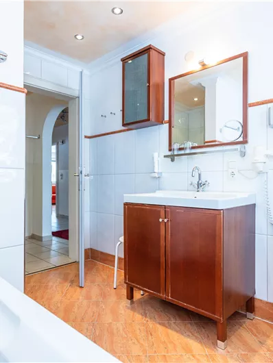 Een moderne badkamer met een houten commode en een wastafel. De muren zijn licht betegeld en er zijn schone handdoeken.