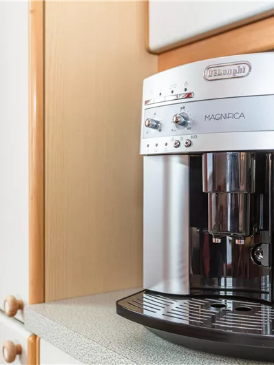 Een moderne koffiezetapparaat in een heldere keukenomgeving. Het heeft een zilveren oppervlak en talloze bedieningsknoppen.