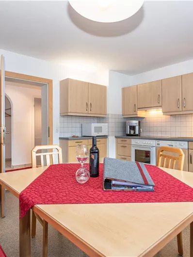 Een heldere keuken met houten meubels en modern design. Op de tafel ligt een rood tafelkleed en een fles wijn.