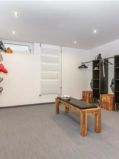 Een moderne skiruimte met ski's en uitrusting die aan de muur hangen. In de ruimte bevinden zich houten rekken en een bank om op te zitten.