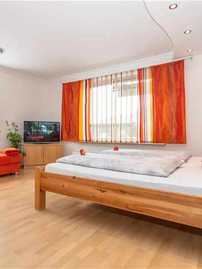 Een knusse kamer met houten meubels en een rode bank. Het raam laat veel licht binnen en er zijn decoratieve kussens.