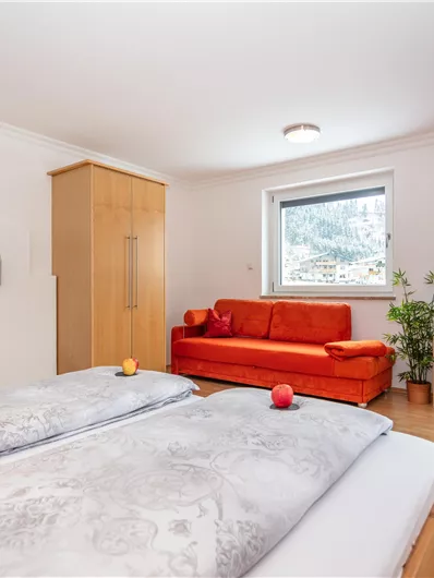 Een gezellige slaapkamers met een tweepersoonsbed en een rode bank. Er is een televisie en uitzicht naar buiten door het raam.