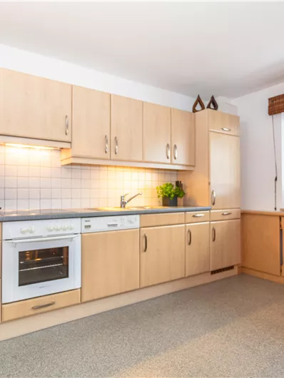 Een lichte keuken met houten kasten en moderne apparaten. Een tafel met rode stoelen en veel natuurlijk licht door het raam.