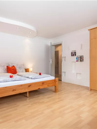 Een lichte slaapkamer met twee eenpersoonsbedden en een houten kast. De muren zijn overwegend wit, met kleurrijke accenten en een gezellige fauteuil.