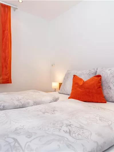 Een gemütelijke slaapkamer met twee bedden en kleurrijke gordijnen. Op een van de kussens ligt een oranje decoratieve hoes.