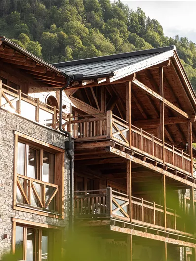 A modern wooden building in the midst of a green mountain landscape. The building has large balconies and offers a beautiful view of nature.