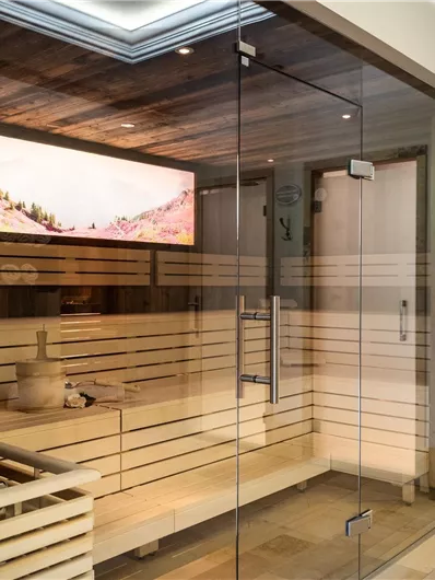 A modern sauna with wooden paneling and large glass fronts. In the background, there is a beautiful screen displaying landscape pictures.