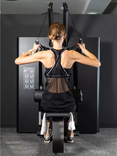 A person is training on a modern fitness machine. The environment is dark and simple, which promotes concentration on the workout.