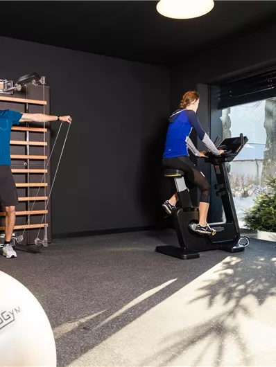 A modern gym with two people working out. One person is using a treadmill while the other is training with resistance bands.