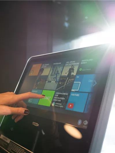A fitness device with a touchscreen displaying various options. One hand is tapping on the screen while sunlight is shining in.