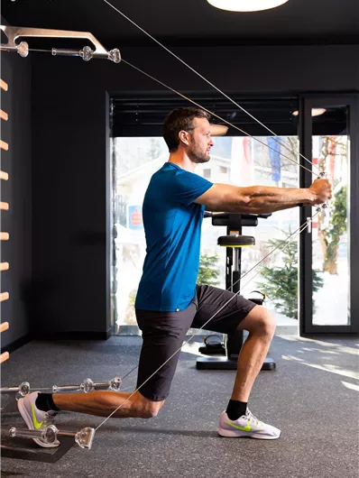 A man is doing an exercise with resistance bands in a modern gym. He is wearing athletic clothing and focusing on his technique.