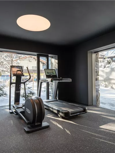 A modern fitness room with a treadmill and cross-trainer. Large windows offer a view of the snowy landscape outside.