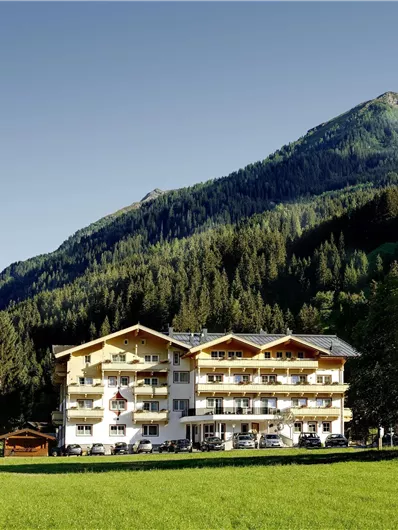 Ein charmantes Gebäude inmitten einer malerischen Berglandschaft. Grüne Wiesen und hohe Tannenbäume umgeben das Hotel.
