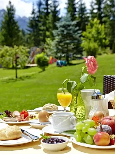 Een uitgebreid ontbijt in de buitenlucht met vers fruit, broodjes en drankjes. De omgeving is groen en zonnig, ideaal voor een ontspannen start van de dag.