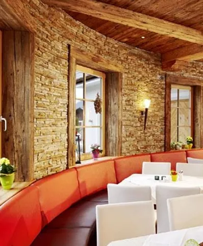 A stylish restaurant with a warm stone wall and wooden ceilings. The tables are elegantly set and offer an inviting atmosphere.