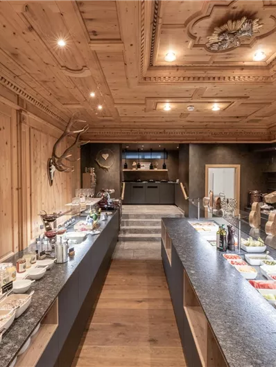 Ein einladender Raum mit Holzinterieur und beleuchtetem Buffet. Auf dem Tisch sind verschiedene Speisen und Getränke angerichtet.