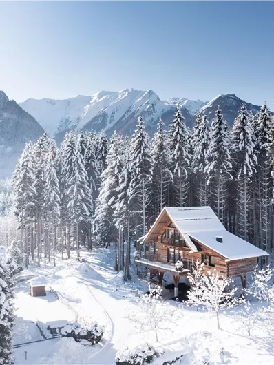 Een schilderachtig berglandschap in de winter met met sneeuw bedekte bomen. Een knus houten huis staat te midden van de besneeuwde natuur.