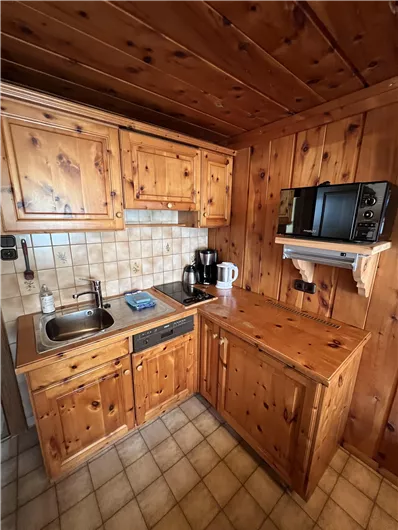 A cozy wooden kitchen with a stove, a sink, and various kitchen appliances. The floor is tiled and the walls are also made of wood.